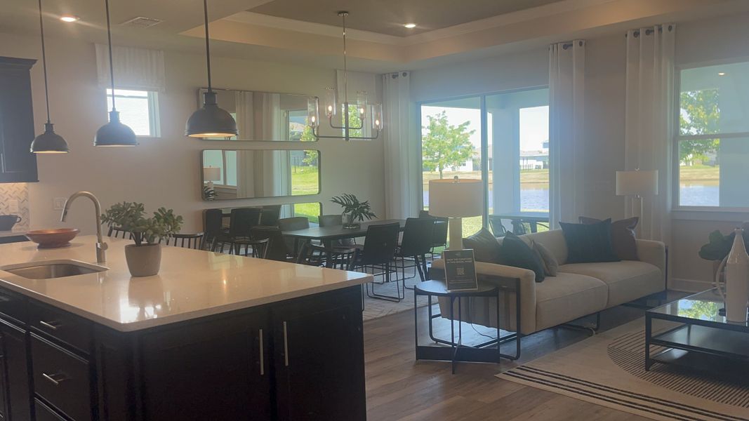 A chic open-plan living area with modern lighting, dark cabinets, and large windows offering serene natural views.