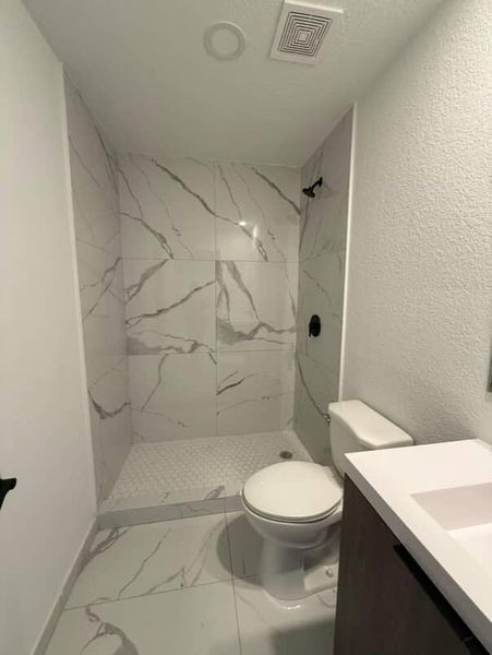 A modern bathroom with sleek marble tiles, a walk-in shower, and a compact vanity.