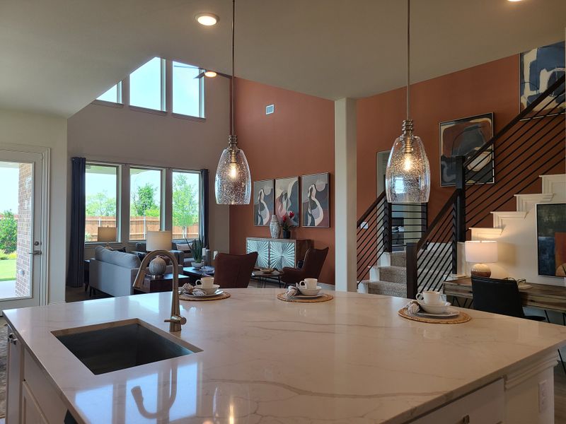 A bright open-concept living area with high ceilings, modern lighting, and large windows overlooking a lush backyard.