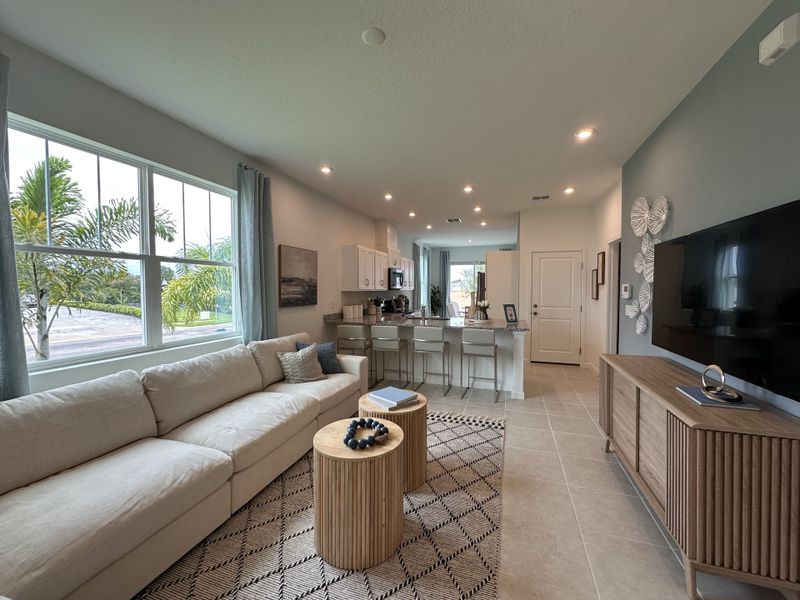A modern living area with a plush sofa, stylish decor, large window, and open kitchen design.