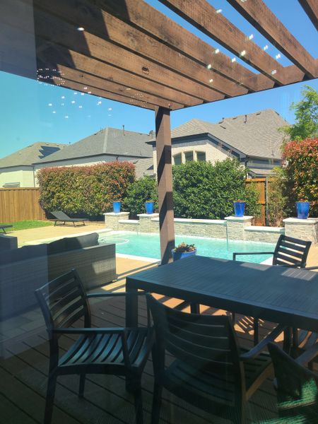 A backyard oasis with a cozy patio, sleek dining set, and sparkling pool under a wooden pergola.