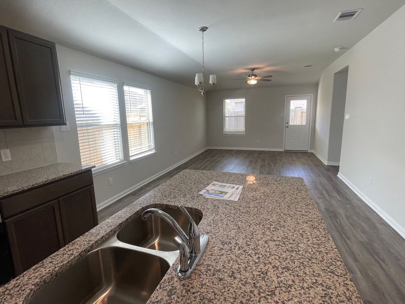 An open-concept kitchen and living area featuring wood floors, granite countertops, modern fixtures, and ample natural light.