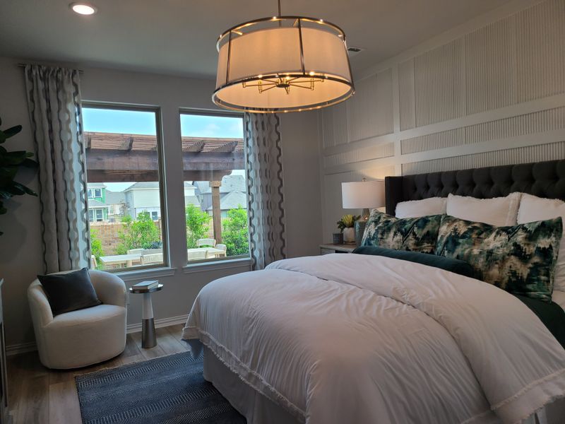 Cozy bedroom featuring a plush bed with patterned pillows, elegant chandelier, and large windows offering natural light and views.