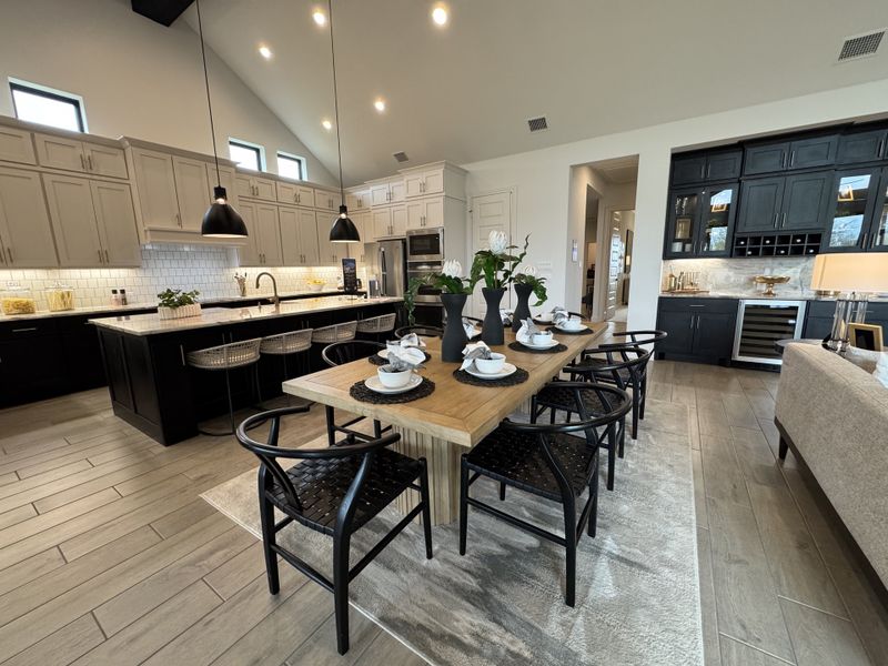 A spacious kitchen-dining area with sleek black cabinetry, a natural wood table, and elegant pendant lighting. A spacious kitchen-dining area with sleek black cabinetry, a natural wood table, and elegant pendant lighting.