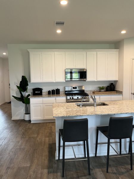 A modern kitchen with white cabinetry, granite countertops, and sleek black stools on wood flooring. A modern kitchen with white cabinetry, granite countertops, and sleek black stools on wood flooring.