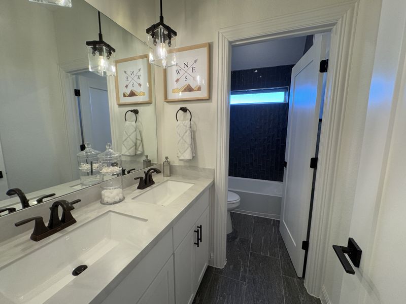A modern bathroom with dual sinks, sleek black fixtures, pendant lighting, and elegant framed artwork. A modern bathroom with dual sinks, sleek black fixtures, pendant lighting, and elegant framed artwork.