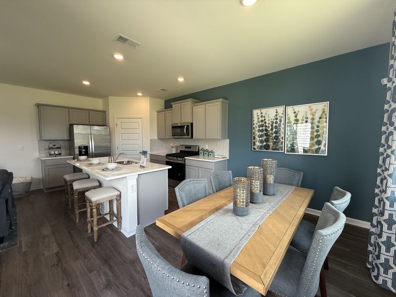 A modern kitchen-dining area with elegant gray cabinetry, stylish decor, and a wooden table setting.
