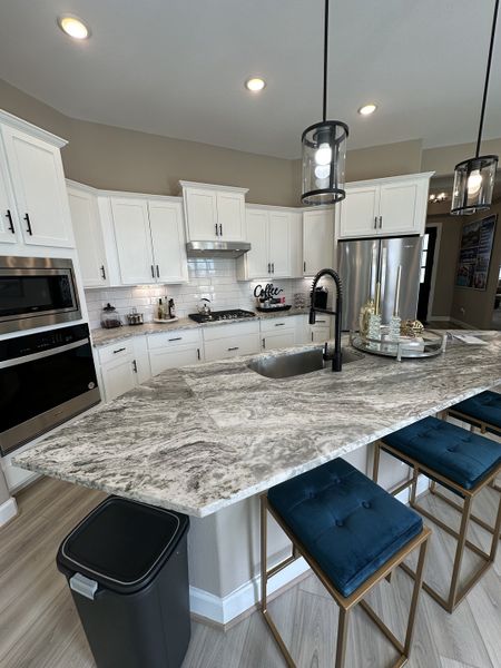 Modern kitchen with white cabinets, granite countertops, sleek appliances, and blue barstools under elegant pendant lighting. Modern kitchen with white cabinets, granite countertops, sleek appliances, and blue barstools under elegant pendant lighting.