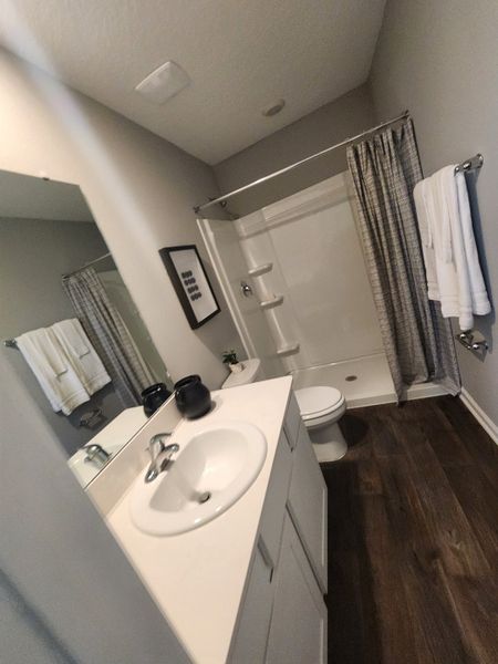 A modern bathroom with sleek fixtures, a single vanity, and a spacious shower on rich wood-look flooring. A modern bathroom with sleek fixtures, a single vanity, and a spacious shower on rich wood-look flooring.