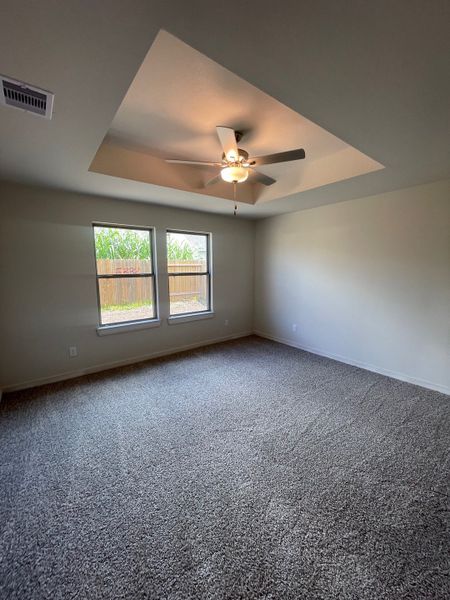 A spacious room with plush carpet, large windows, and a ceiling fan, offering comfort and natural light.