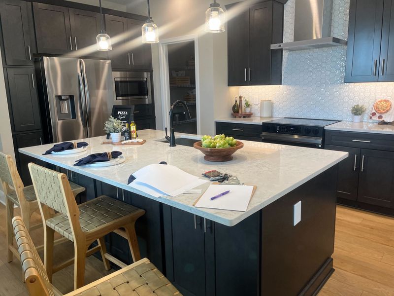 A modern kitchen with dark cabinets, a spacious island, stainless steel appliances, and elegant pendant lighting. A modern kitchen with dark cabinets, a spacious island, stainless steel appliances, and elegant pendant lighting.