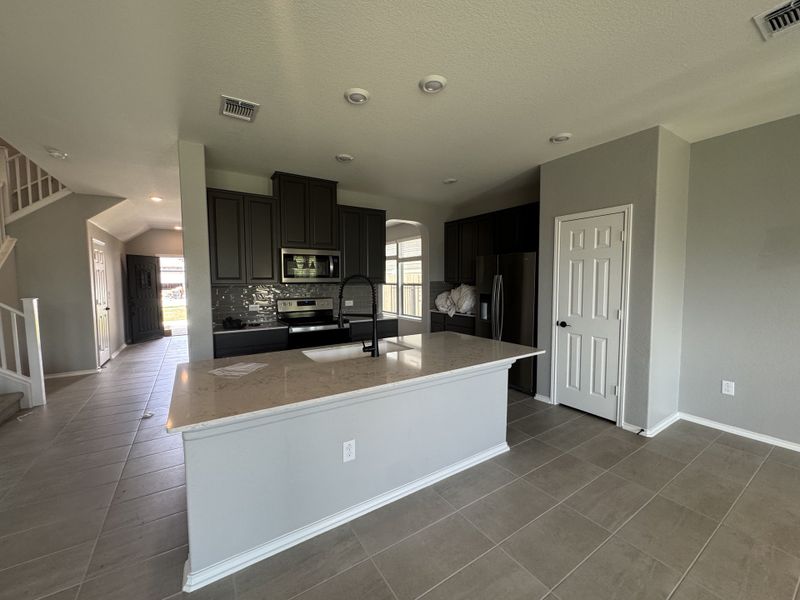 A modern kitchen featuring sleek dark cabinets, a central island with marble countertop, and stainless steel appliances.