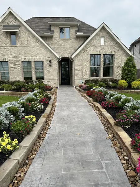 A charming brick home with manicured gardens and a stone path in The Meadows at Imperial Oaks 40' - Section 20 by Coventry Homes (Conroe, TX).
