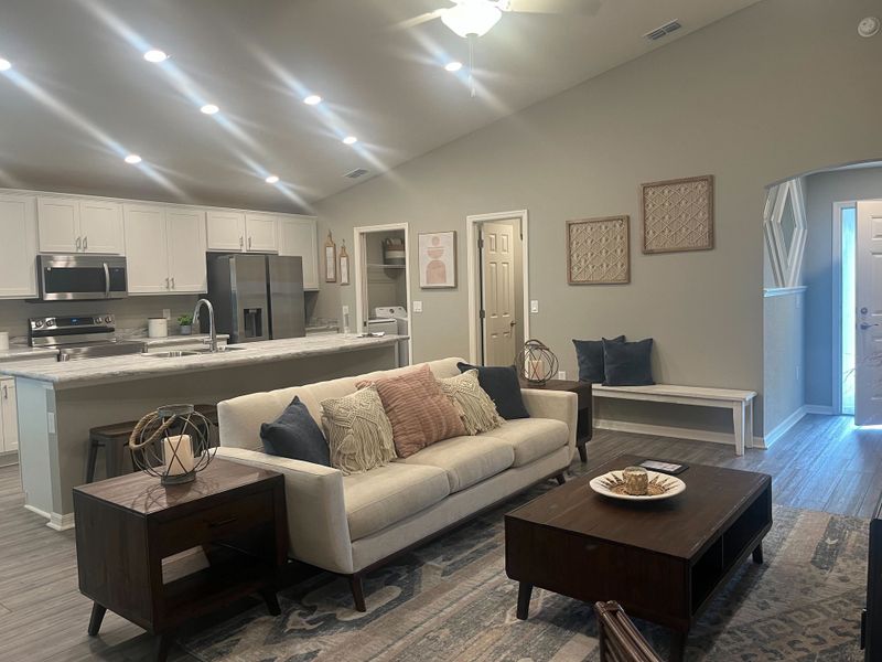 An inviting living room featuring an open kitchen, cozy sofa, and elegant decor with warm lighting and wooden accents. 