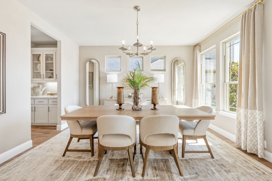 Dining room with wood table, upholstered chairs, chandelier, and large windows with neutral curtains Dining room with wood table, upholstered chairs, chandelier, and large windows with neutral curtains