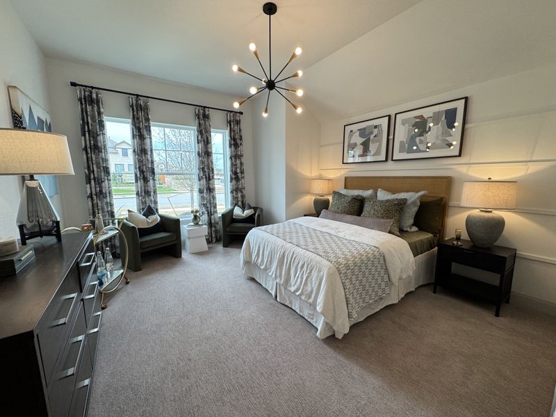 A cozy bedroom featuring a modern chandelier, elegant decor, large windows, and a plush bed with stylish bedding.