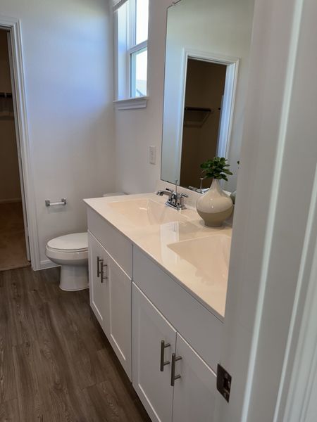 A sleek bathroom with a large mirror, white cabinets, laminate flooring, and modern fixtures.