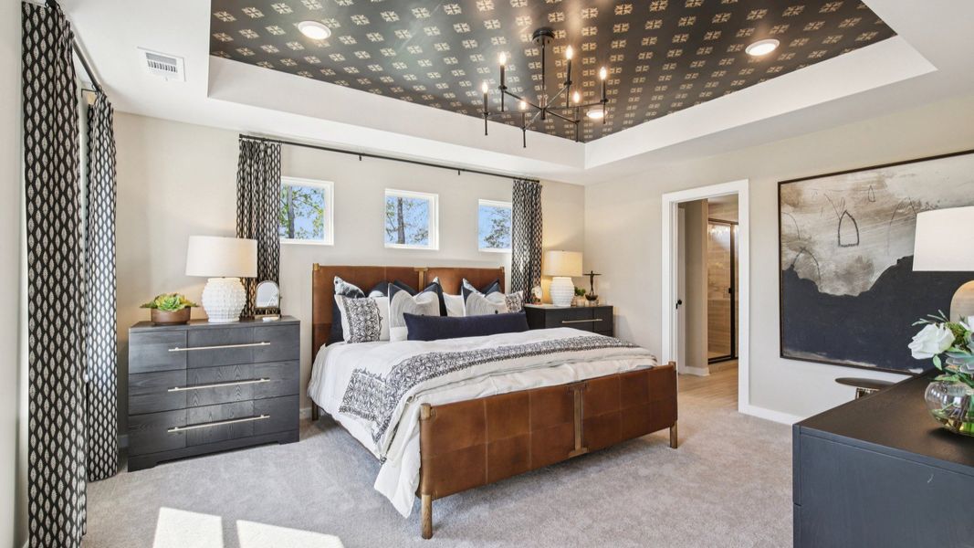 Large primary bedroom with natural light, accent tray ceiling, and en-suite bathroom