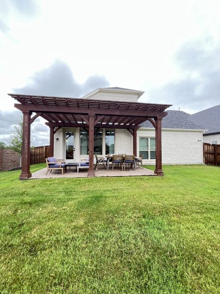 A lovely white brick home with a wooden pergola and lawn in Edgewater by Grand Homes (Fate, TX).