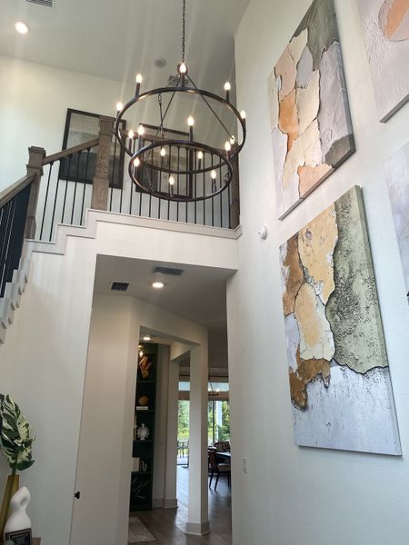 A modern entryway featuring a grand chandelier, abstract wall art, and an open hallway leading to a sunlit living space.