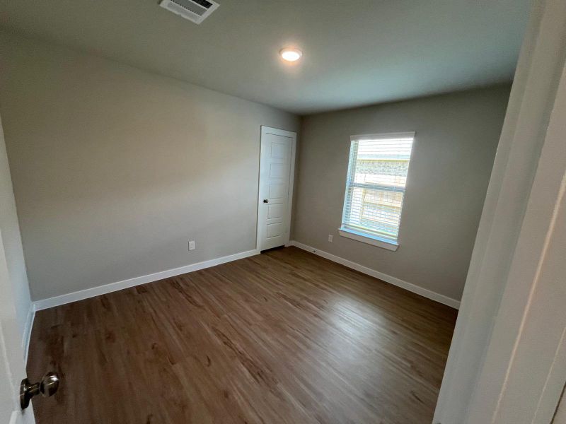 A cozy room with wood flooring, neutral walls, and a window offering natural light, perfect for versatile design.