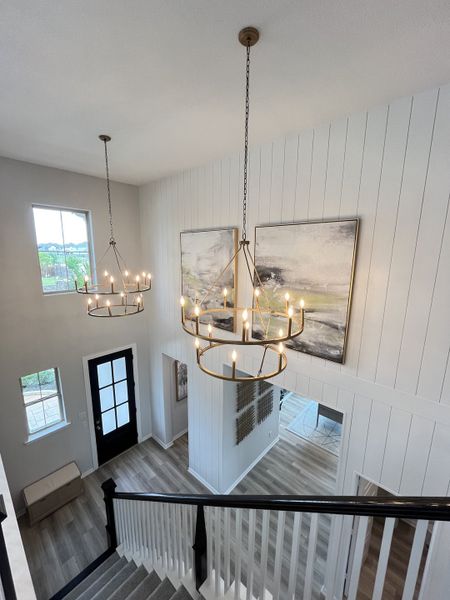 An elegant entryway with dual chandeliers, modern accents, and hardwood floors creates a welcoming and stylish atmosphere.