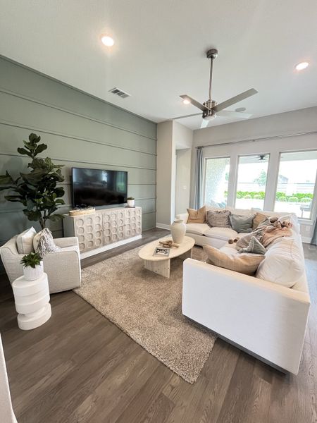 A cozy living room featuring a sectional sofa, stylish TV console, plush rug, and modern ceiling fan with soft lighting.
