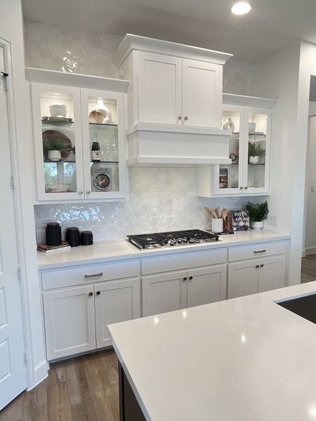 A sleek kitchen with white cabinetry, hexagonal tile backsplash, and modern cooktop on quartz countertops. A sleek kitchen with white cabinetry, hexagonal tile backsplash, and modern cooktop on quartz countertops.