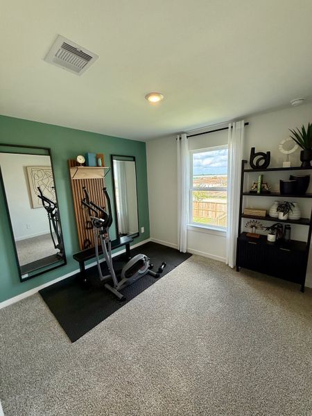 A modern exercise room with a stationary bike, full-length mirrors, and a stylish green accent wall.