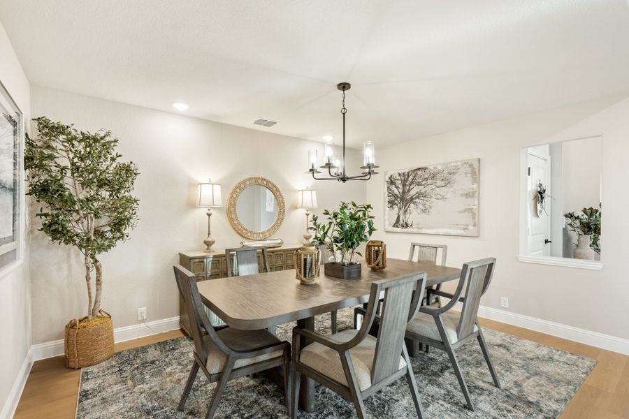 Dining room with wood table, six chairs, chandelier, and patterned area rug on hardwood floors