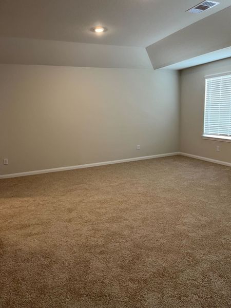 A spacious room with soft carpeting, neutral walls, recessed lighting, and a large window with blinds.