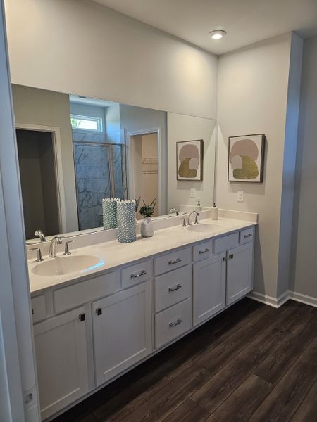 A modern bathroom with a dual vanity, elegant white cabinets, and stylish wall art, complemented by a spacious shower area.