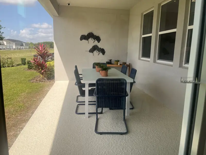 A cozy patio with a sleek white table, blue chairs, and potted plants, perfect for outdoor dining and relaxation.