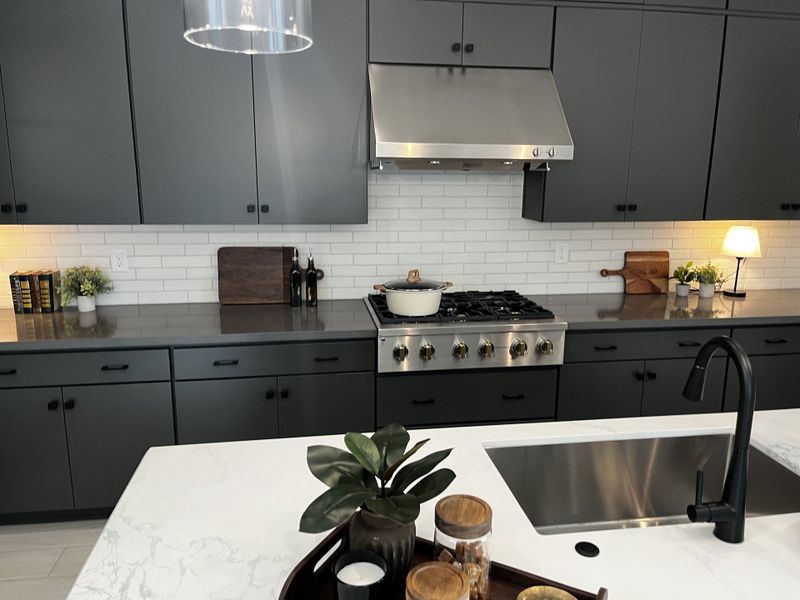 Contemporary kitchen with dark cabinetry, a gas range, and elegant white countertops.