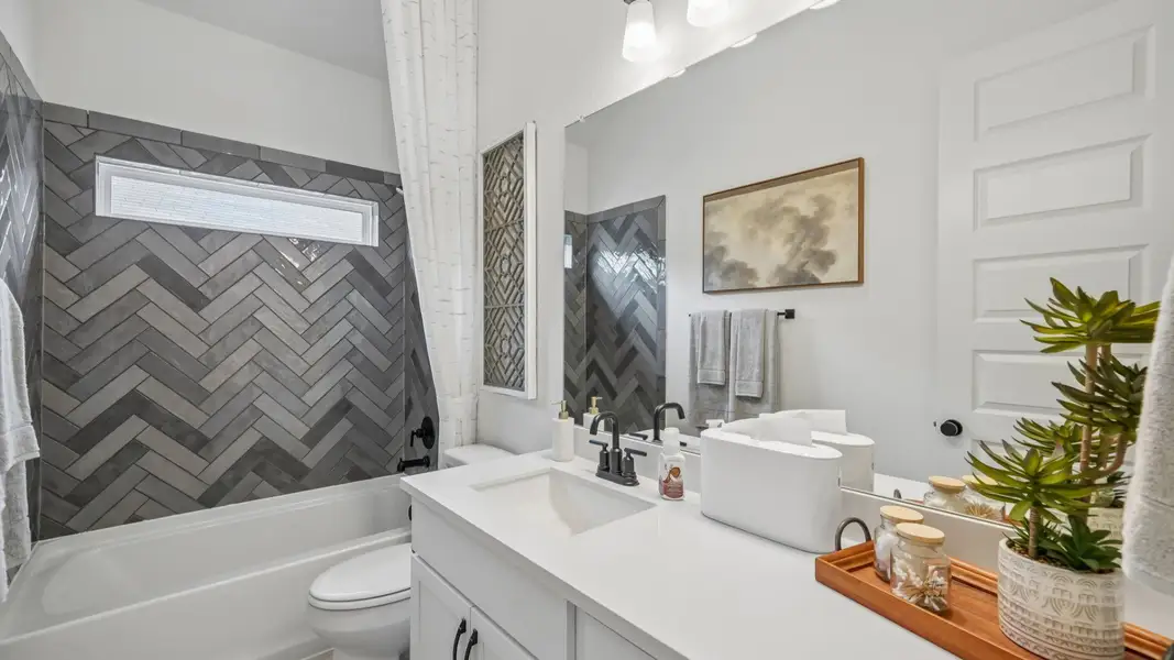 Secondary bedroom featuring gray tile tub/shower combo, natural light window, and single vanity with spacious counter Secondary bedroom featuring gray tile tub/shower combo, natural light window, and single vanity with spacious counter