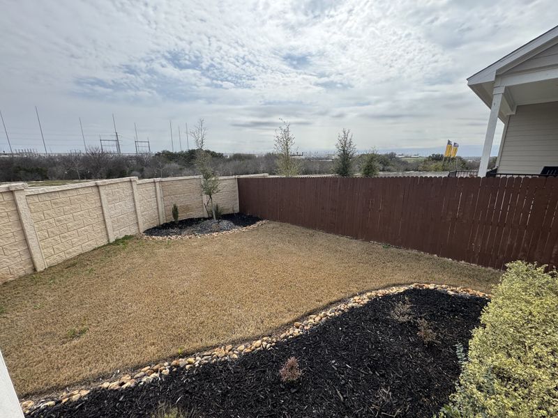 A spacious backyard with stone-edged landscaping in Hunters Ranch by First America Homes, San Antonio, TX.