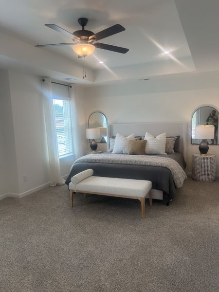 A cozy bedroom with plush carpeting, a cushioned bench, and a modern ceiling fan for a serene, inviting atmosphere. A cozy bedroom with plush carpeting, a cushioned bench, and a modern ceiling fan for a serene, inviting atmosphere.