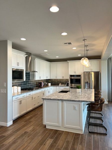 Modern kitchen with white cabinets, marble island, black tile backsplash, and wood flooring. Bright and spacious layout.