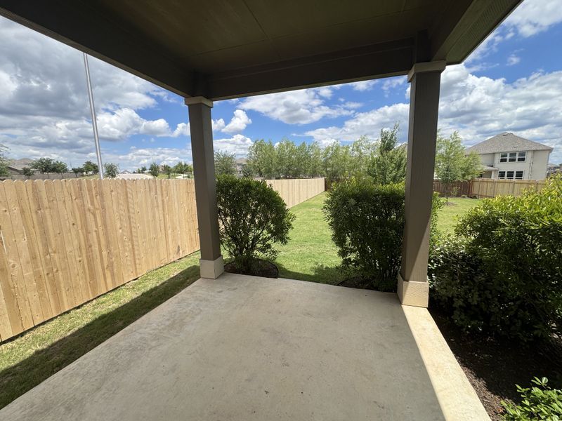 A covered patio overlooking a lush green backyard with a wooden fence and clear skies.