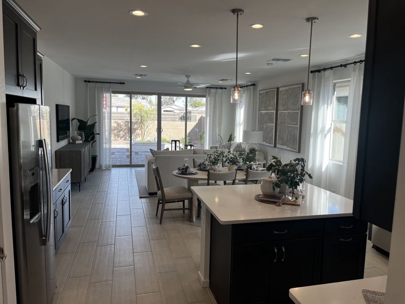 Elegant kitchen with dark cabinets, white countertops, and pendant lights opening into a well-lit dining and living space.