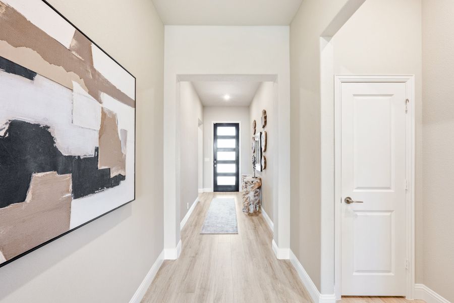 Hallway with light wood floors, white walls, black front door, and large abstract wall art