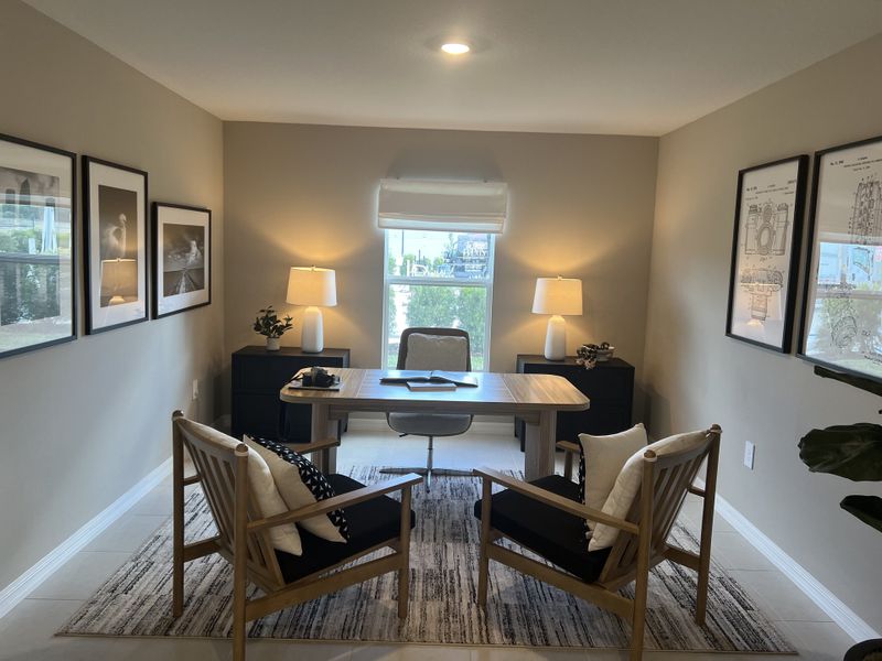 A cozy home office with elegant framed art, a sleek wooden desk, modern chairs, and soft lighting.