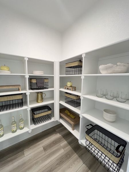 A well-organized pantry with white shelving, stylish wire baskets, and modern wooden flooring.