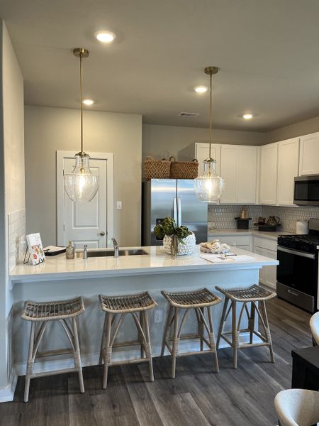 A modern kitchen with sleek white cabinets, pendant lighting, and woven stools at a spacious island.