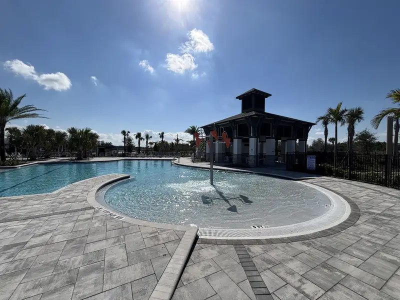 A resort-style pool with a covered pavilion, palm trees, and ample lounge seating in Eden at Crossprairie by M/I Homes (St. Cloud, FL).