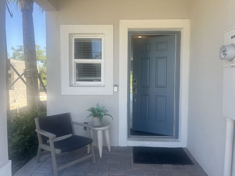 A cozy front porch with a blue door, black chair, and potted plant on a small table.