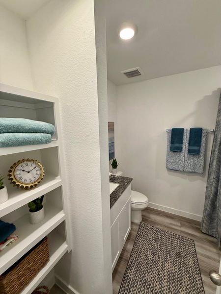 A cozy bathroom with sleek shelving, soft towels, and elegant decor. Features a granite countertop and a stylish patterned rug.