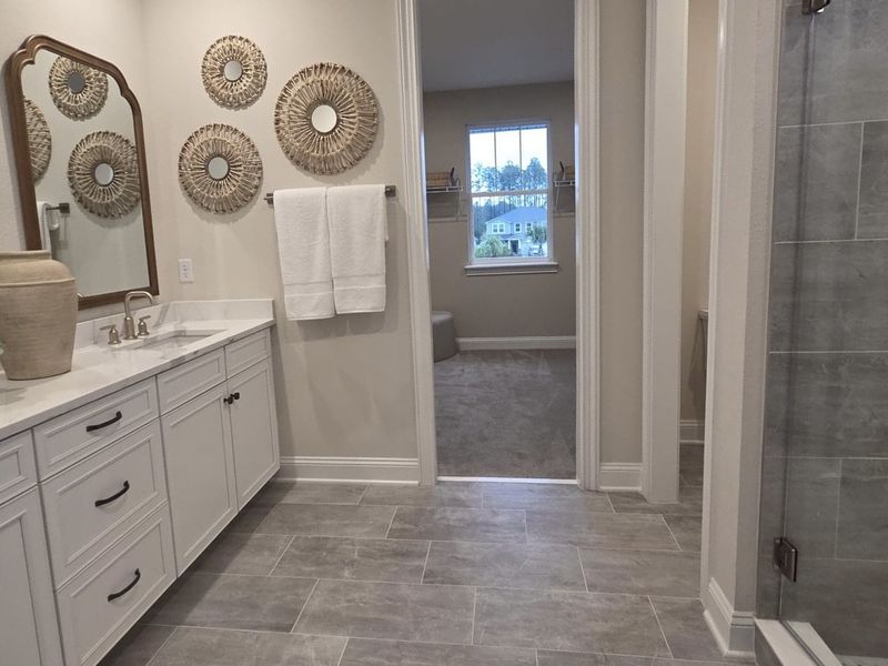 Elegant bathroom featuring a sleek vanity, woven wall decor, and a spacious layout with a view of carpeted space beyond. Elegant bathroom featuring a sleek vanity, woven wall decor, and a spacious layout with a view of carpeted space beyond.