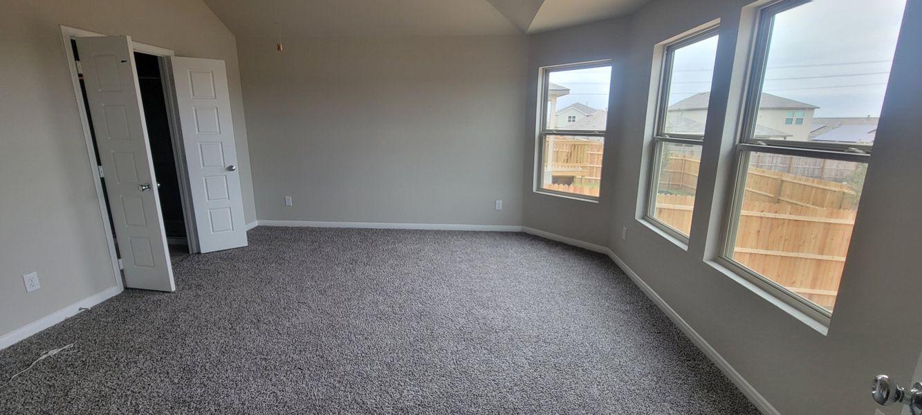 A spacious bedroom with soft carpet, large windows, and an open closet offering ample natural light and cozy comfort.