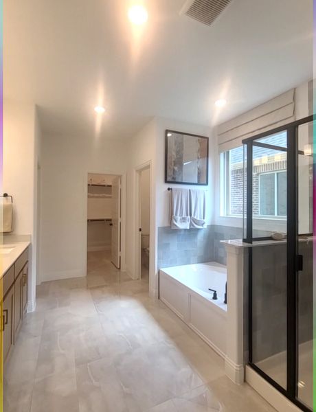 A spacious bathroom with sleek tiles, a glass shower, built-in tub, and elegant lighting.